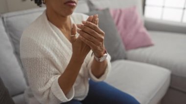 Oturma odasında oturan Afrikalı bir Amerikalı kadın endişeli bir ifadeyle bileğine masaj yapıyor..