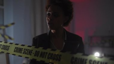 Siyahi bir kadın dedektif, loş ışıkta yanan bir suç mahallinde kanıtları analiz ediyor.