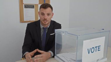Takım elbiseli genç bir adam oy sandığının yanında konuşuyor.