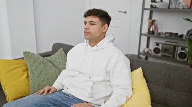 Gündelik giysiler içinde kuşkucu genç bir Arap, evinde kollarını kavuşturup gergin ve olumsuz yüz ifadesini tasvip etmiyor.