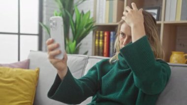 Kafkasyalı genç bir kadın rahat bir oturma odasında akıllı telefonuyla selfie çekiyor..