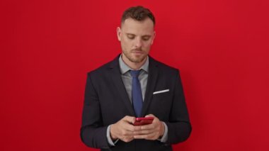 Kızgın İspanyol takım elbiseli genç adam, akıllı telefondan öfkeyle bağırıyor, öfkeli ve hayal kırıklığına uğramış, izole edilmiş kırmızı arka planda öfke ve saldırganlık yayıyor.