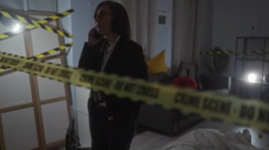 Telefondaki orta yaşlı kadın dedektif evdeki suç mahallini dikkatli bant ve kanıt işaretleriyle araştırıyor..