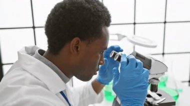 Modern bir laboratuvar ortamında mikroskop kullanan odaklanmış Afrikalı bilim adamı.