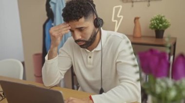 Sakallı, stresli bir İspanyol modern ofis ortamında dizüstü bilgisayarla çalışır. Hayal kırıklığı ya da baş ağrısı gösterir..