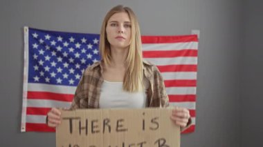 Amerikan bayrağının önünde çevreci bir mesaj taşıyan karton tabela tutan sarışın kadın.
