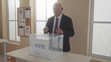 Kafkasyalı yaşlı bir adam demokratik katılım ve vatandaşlık görevini betimleyen bir üniversite odasındaki oy sandığında oyunu kullanıyor..