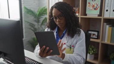 Modern bir klinikte tablet kullanan Afrikalı, Amerikalı, kadın doktor. Arka planda bilgisayar ve bitkiler var..