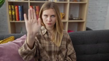 Kanepede oturan genç sarışın kadın avuç içiyle şarkı söylemeyi kesiyor. Yüzünde olumsuz ve ciddi bir jest olan uyarı ifadesi. evde.
