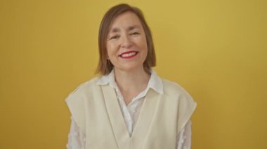 Kendine güvenen orta yaşlı İspanyol kadın sarı arka planda tek başına duruyor. Yürek ısıtan bir gülümsemeyi paylaşırken mutlu görünüyor.