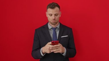 Takım elbiseli İspanyol genç adam stres ve üzüntüye yenik düştü, ağladı ve kederlendi. Akıllı telefonunu izole edilmiş kırmızı arka plana karşı kullandı.