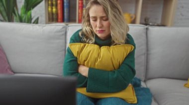 Sıkıntılı genç bir sarışın kadın evde oturur, bir kanepede yastığa sarılır, hüzün ve yalnızlık temalarını anımsatır..