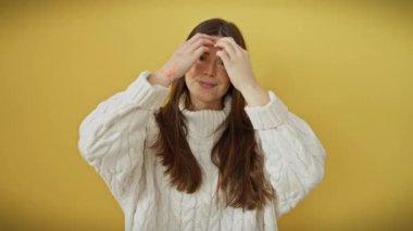 Kendine güvenen, modaya uygun süveter giymiş genç İspanyol kadın, izole edilmiş sarı arka planda saçlara dokunuyor, seksi, neşeli ve çekici bir güzellik ve tarz gösterisi yapıyor.