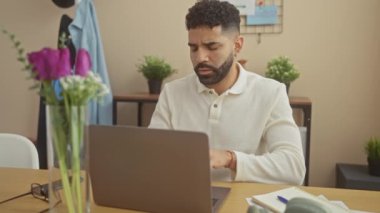 İspanyol bir adam, modern bir apartman dairesinde dizüstü bilgisayarıyla çalışırken omuz ağrısı çekiyor..