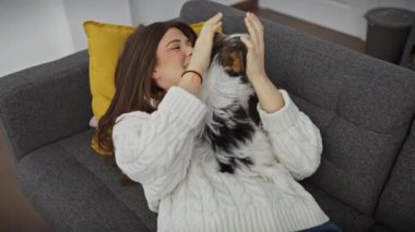 Genç bir kadın, gri bir kanepede bisikletli teriyeriyle sarılıp, rahat bir oturma odasında keyif çatıyor..