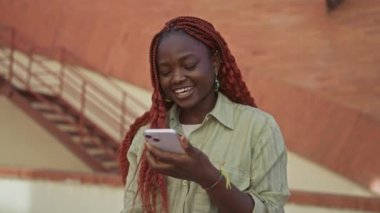 Kentsel caddede akıllı telefon kullanan mutlu Afrikalı kadın.