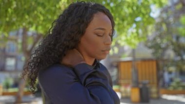 Genç Afro-Amerikalı kıvırcık saçlı kadın şehir parkında boyun ağrısı çekiyor..