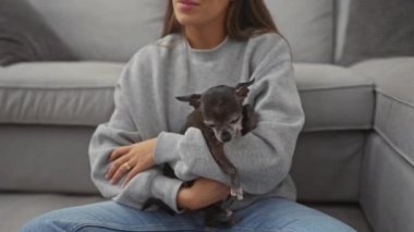Rahat giyimli genç bir kadın uykulu chihuahua 'sını evin içinde rahat bir kanepeye yatırır..
