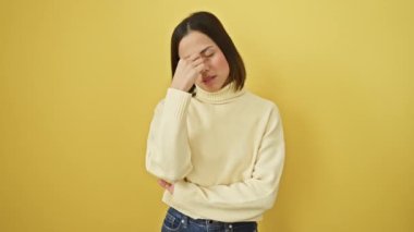 Süveter giyen, burnu ve gözleri ovuşturmaktan yorgun düşmüş, yorgun ve başı ağrıyan genç ve güzel bir İspanyol kadın. Stres ve hüsran kavramı. izole edilmiş sarı arkaplan