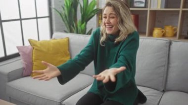 Kanepede oturan genç sarışın kadın parmağını yan tarafa uzatıp gülümsüyor evde ağzı açık mutlu bir şekilde.