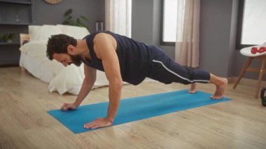 Orta yaşlı sakallı bir adam yatak odasında yoga minderi üzerinde egzersiz yapıyor. Güç ve esneklik gösteriyor..