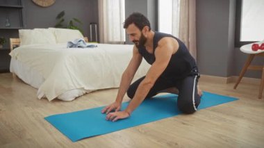 Modern bir yatak odasında yoga minderinin üzerinde uzanan bir adam sağlıklı bir yaşam tarzı ve ev egzersizleri sergiliyor..
