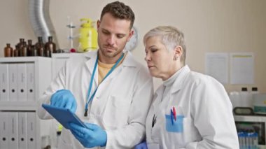 Laboratuvar önlüklü bir adam ve kadın, iyi donanımlı bir laboratuarda tabletteki verileri analiz ediyorlar..