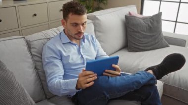 Oturma odasında oturan genç bir İspanyol kanepeye oturmuş heyecanını ve coşkusunu gösteren bir tablet kullanıyor..