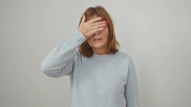 Süveter giymiş orta yaşlı güzel bir kadın neşeyle gözlerini eliyle kapatıyor, şaşırmak için kör. Beyaz arka planda tek başına duruyor, güvenle gülümsüyor..