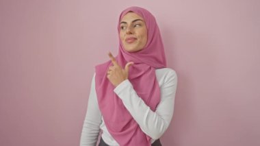 Neşeli genç İspanyol kadın, tesettürlü, mutlu bir gülümsemeyle yukarıya bakıyor. İzole edilmiş pembe bir duvarın üzerinde büyülenmiş, saf mutluluktan başka bir şey sunmayan.