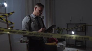 Kravatlı dedektif, gece vakti olay yerindeki tablet üzerindeki kanıtları dikkatli bir bant ve ortam aydınlatmasıyla inceliyor..
