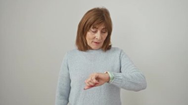 Süveter giyen, kendinden emin orta yaşlı bir kadın, tek başına ayakta duruyor, beyaz izole bir arka planda havalı bir iş adamı mien ile kol saatini kontrol ediyor. Asla geç kalmaz..