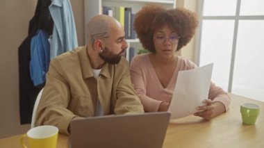 Irklar arası çiftler ev ofisinde laptoplar ve kahveyle gazete tartışıyorlar.