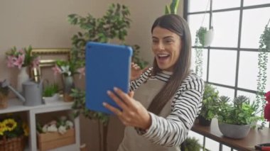 Neşeli bir kadın evde bahçeyle uğraşmaktan zevk alır, tabletindeki arkadaşlarıyla bitkilerle dolu sıcak bir oturma odasında görüntülü sohbet eder..