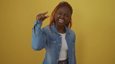 Kızgın Afro-Amerikalı kadın, kot gömlekli, hoşnutsuz ve öfkeli, kameradan size bakıyor, sarı bir arka planda izole edilmiş.