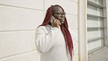 Kırmızı örgülü ve gözlüklü Afro-Amerikalı kadın şehir içi telefon görüşmesinde.