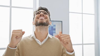 Sakallı, neşeli, genç, İspanyol bir adam ofis içinde başarıyı kutluyor..