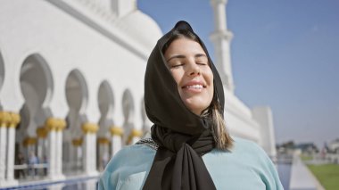 Hiyerarşik giyinmiş genç bir İspanyol kadın Abu Dabi 'deki bir camide huzur içinde gülümsüyor..