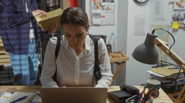 Odaklanmış kadın araştırmacı masasında çalışıyor. Karışık bir dedektiflik ofisinde erkek bir meslektaşla birlikte..