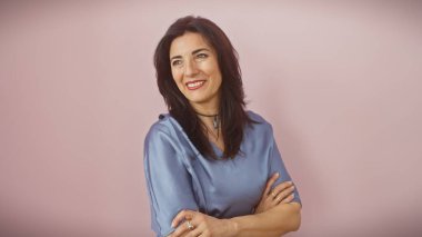 Kollarını kavuşturup pembe bir arka plana gülümseyen olgun İspanyol kadın.