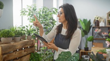 Parlak bir çiçekçinin içindeki çeşitli bitkilerin arasında tablet kullanan İspanyol kadın.