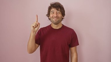 Sakallı, pembe izole edilmiş bir arka plana bakan neşeli, genç bir İspanyol. Günlük bordo bir gömlek giyiyor..