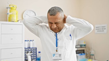 Laboratuvar kıyafeti giymiş orta yaşlı bir İspanyol klinik hastane ortamında stres ya da baş ağrısı yaşar..