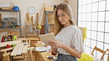 Genç bir kadın, iyi aydınlatılmış bir marangozluk atölyesinde dizayn ve planlama üzerine ipucu veren bir defter inceliyor..