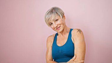 Kendine güvenen, orta yaşlı, gri saçlı, pembe arka planda poz veren mavi bluzlu İspanyol bir kadın..