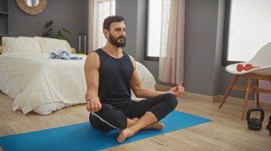 Olgun sakallı bir adam yatak odasının içindeki yoga minderinde meditasyon yapıyor. Sükunet ve huzuru temsil ediyor..