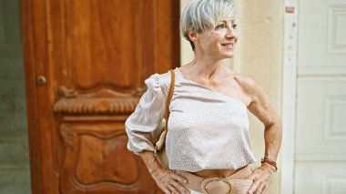 Gri saçlı olgun bir kadın yeni evinin ön kapısının önünde duruyor. Güzelliği ve kendine güveni somutlaştırıyor..