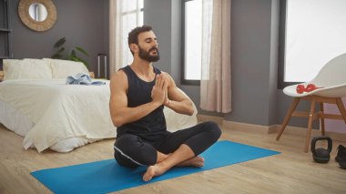 Orta yaşlı bir adam, modern bir yatak odasında huzur içinde yoga yapar..