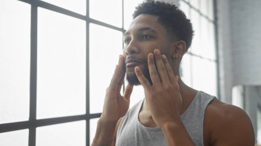 Yakışıklı siyahi adam güneşli, modern bir dairede günlük cilt bakımını yapıyor..