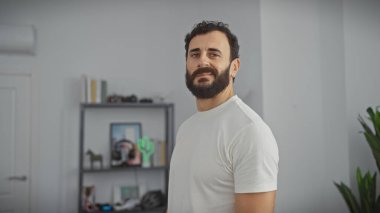 Sakallı, kendine güveni tam bir adam modern bir salonda duruyor ve zarafetini sergiliyor..